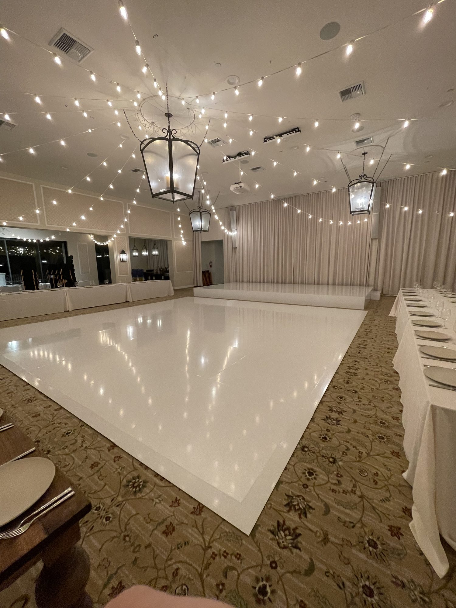 White gloss vinyl dance floor, cut to size and installed in a ballroom under string lights